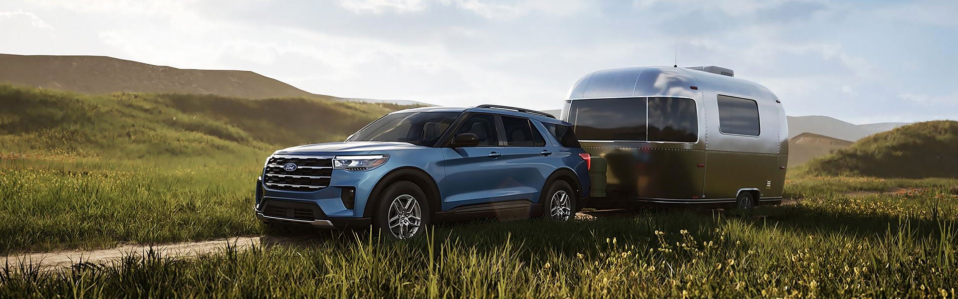Blue Ford Explorer towing a silver camper trailer through a grassy field